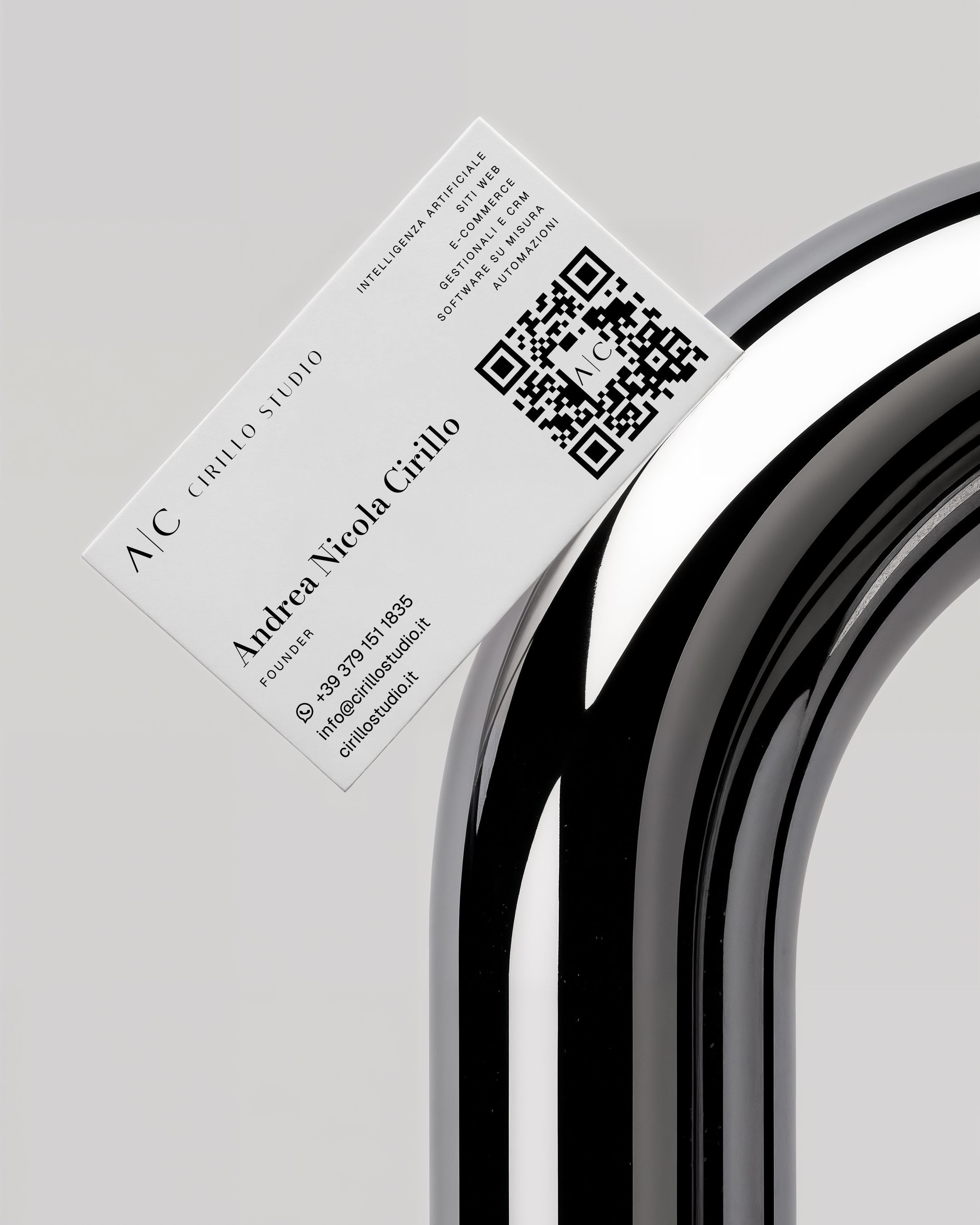 Retro del biglietto di Cirillo Studio con nome, contatti e QR, appoggiato su un tubo cromato.
